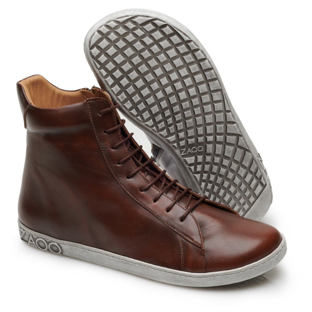 Ein Paar SNAQ Antique Brown High-Top-Sneaker mit weißer Sohle, hergestellt von ZAQQ. Ein Schuh steht aufrecht, während der andere geneigt ist, sodass die Sohle mit Waffelmuster sichtbar ist. Die stylischen Barfußschuh-Sneaker sind an der Seite mit dem ZAQQ-Logo verziert.