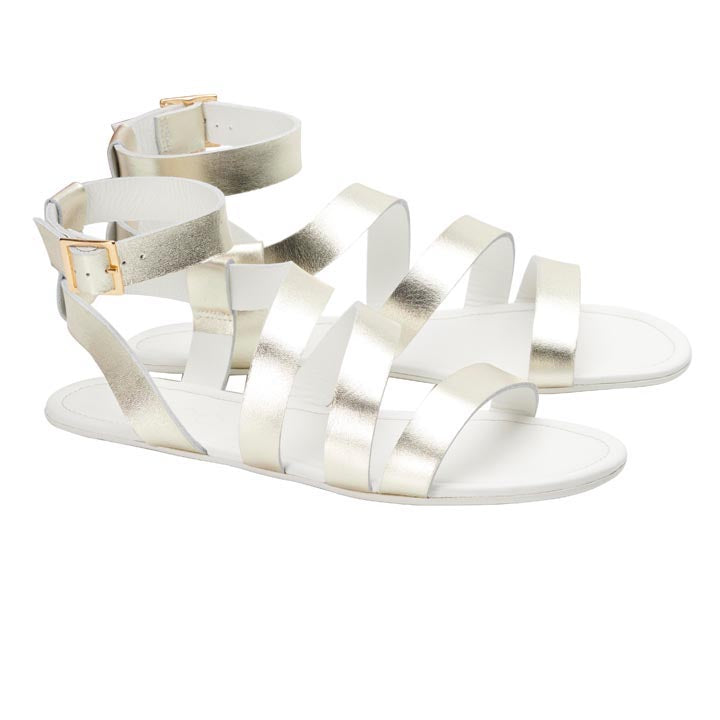 Das Modell MONIQ Champagne von ZAQQ ist ein Paar Sandalen in Metallic-Gold mit mehreren horizontalen Riemen und Knöchelschnallen. Sie sind aus schimmerndem Glattleder gefertigt und eignen sich perfekt, um Ihre Sommeroutfits vor einem weißen Hintergrund aufzuwerten.