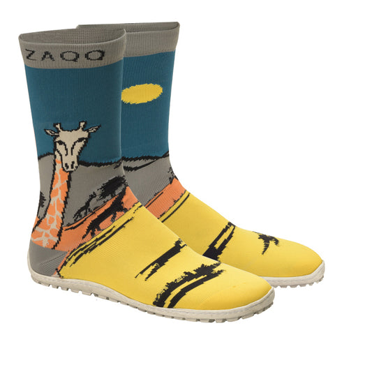 Die SOQQ Giraffe Yellow sind leuchtende Socken von ZAQQ, die wie High-Top-Sneaker aussehen und eine Giraffe inmitten einer sonnenbeschienenen Berglandschaft zeigen. Der Hintergrund zeigt eine Mischung aus blauem, gelbem und orangefarbenem Strickgewebe, wobei die Marke ZAQQ prominent oben abgebildet ist.