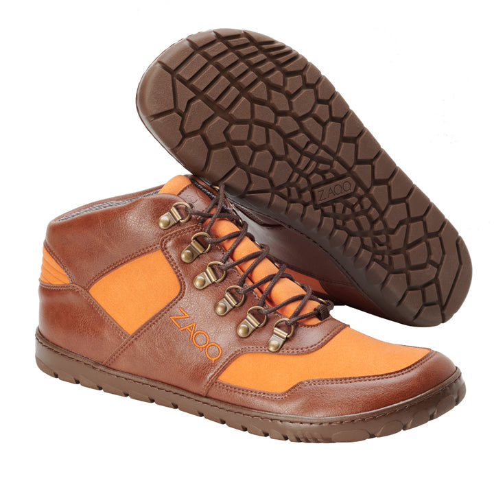 Ein Paar vegane High-Top-Sneaker in Braun und Orange mit strukturierten Gummisohlen, ideal für Outdoor-Abenteuer. Diese Schuhe haben Metallösen, braune Schnürsenkel und tragen stolz „ZAQQ HIQE Mid Vegan Orange“ an der Seite und der Sohle. Sie sind so positioniert, dass sowohl die Ober- als auch die Sohlenansicht zu sehen sind, und sind außerdem wasserdicht.