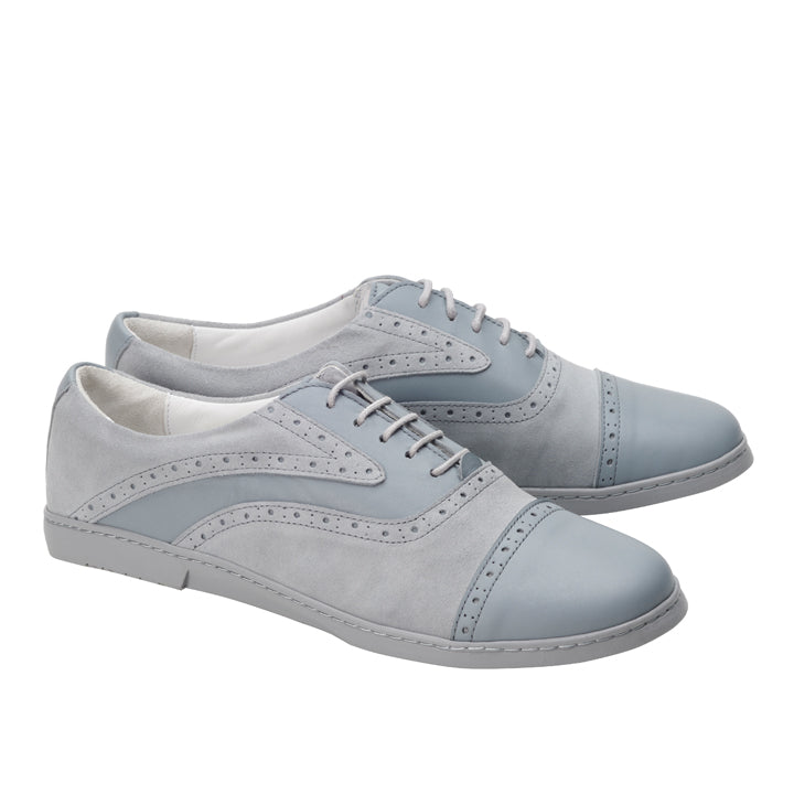 Ein Paar ZAQQs QENTLE Grey Abendschuhe in Hellgrau und Blau, hergestellt aus Velours- und Nappaleder. Diese Businessschuhe sind mit Schnürsenkeln und dekorativen Perforationen versehen und zeigen ein klassisches Design mit sowohl glatten als auch strukturierten Oberflächen, das sich elegant vor einem schlichten weißen Hintergrund präsentiert.