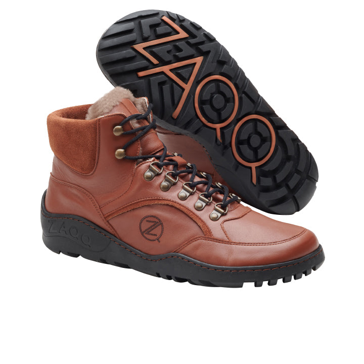 Ein Paar wasserdichte TERRAQ Cognac Winter-Sneaker von ZAQQ, hergestellt aus reichhaltigem Nappaleder im braunen High-Top-Stil, mit schwarzen Gummisohlen. Ein Schuh steht aufrecht, während der andere geneigt ist, um die Sohle freizugeben, und zeigt einen auffälligen ZAO-Schriftzug und kreisförmige Muster, perfekt für diejenigen, die den Komfort von Barfußschuhen schätzen.