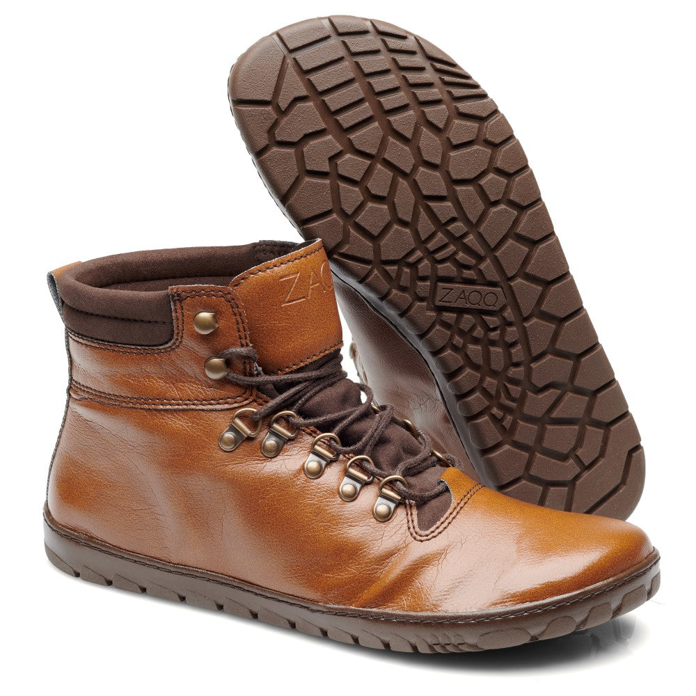 Wir präsentieren die EXPEQ Vegan Cuoio Waterproof-Stiefel von ZAQQ in einem eleganten Design in brauner Lederoptik. Diese Outdoor-Stiefel verfügen über sechs Ösen und Metallhaken zur Sicherung der Schnürsenkel, ergänzt durch einen gepolsterten Schaft für zusätzlichen Komfort. Mit einem geprägten Logo an der Seite und einer strukturierten Außensohle, die sowohl Halt als auch Flexibilität bietet, wird ein Stiefel aufrecht präsentiert, während der andere geneigt ist, um seine Sohle freizugeben.