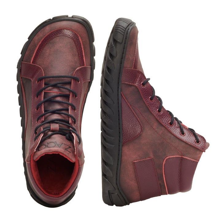 Ein Paar OSQAR Bordeaux High-Top-Sneaker von ZAQQ in sattem Bordeaux mit schwarzen Schnürsenkeln und ULTRAGRIP-Sohlen. Ein Schuh steht aufrecht, während der andere auf der Seite liegt, was die robuste Textur und das stilvolle Design hervorhebt.