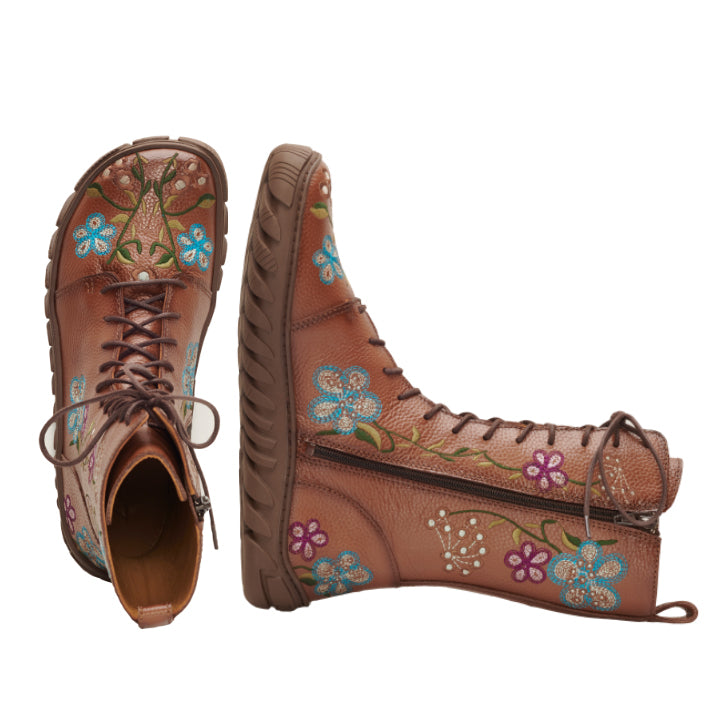 Der DOQS Flower von ZAQQ ist ein Paar brauner Lederstiefel, verziert mit lebendigen Blumenstickereien in Blau-, Rosa- und Weißtönen, die Retro-Charme ausstrahlen. Sie verfügen über Schnürsenkel und dicke, robuste Sohlen – ein Stiefel steht aufrecht, während der andere auf der Seite liegt – und demonstrieren ihr detailliertes Design aus Premium-Nappaleder.