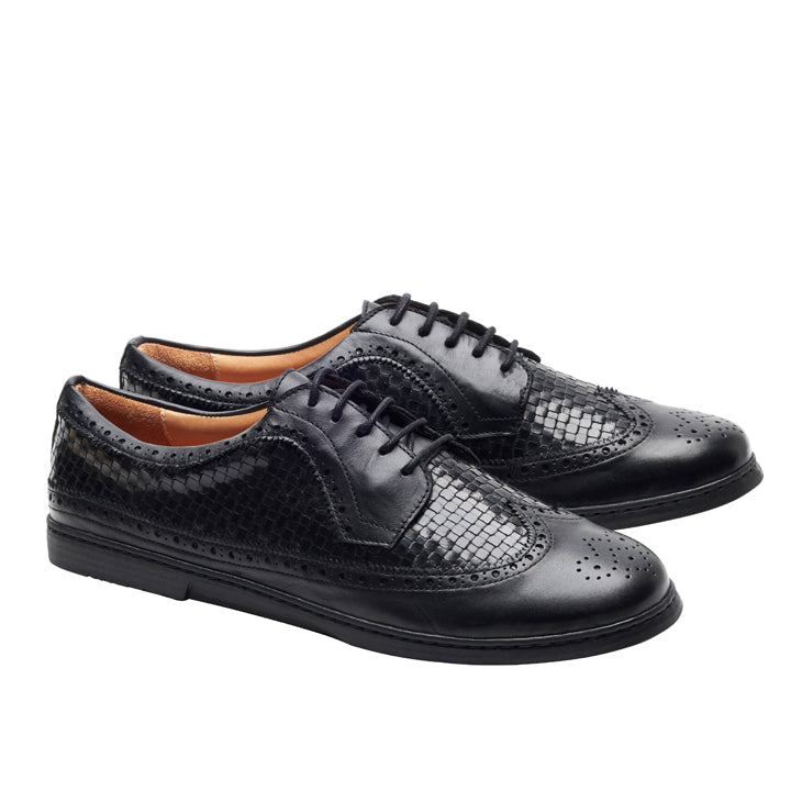 Die ZAQQ BRIQ Brogue Tresse Black Schuhe, gefertigt als anspruchsvoller Businessschuh, zeichnen sich durch ein strukturiertes Schlangenhaut-ähnliches Muster und zeitlose Flügelkappendetails aus. Diese schwarzen Lederbrogues mit Schnürsenkeln heben sich stilvoll von einem schlichten weißen Hintergrund ab.