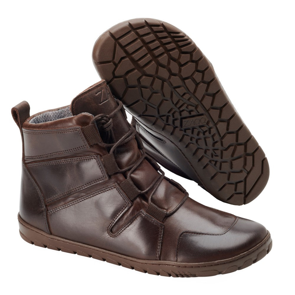 Entdecken Sie den DAQOTA Waterproof Choco von ZAQQ, braune High-Top-Schuhe mit dunkelbrauner Sohle, verstellbaren Riemen und aufwendigen Nähdetails. Mit einem Schuh, der aufrecht steht, und dem anderen, der seine strukturierte Sohle zeigt, bieten diese eleganten Barfußschuhe ein modernes Design und ein innovatives wasserdichtes Erlebnis.