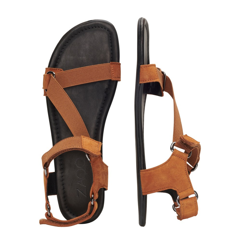 Abgebildet sind zwei MIQA Brown Barfußsandalen von ZAQQ mit schwarzer Sohle. Eine Sandale ist von der Seite und die andere von oben zu sehen, wodurch das verstellbare Riemensystem und das lässige Design aus hochwertigem Wildleder hervorgehoben werden.