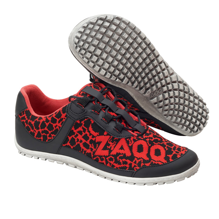 Die QASEY Red Sneaker von ZAQQ sind aus schwarzem und rotem Mesh-Gewebe gefertigt. Diese veganen Barfußschuhe zeichnen sich durch ein strukturiertes Design mit schwarzen Overlays auf Rot aus und tragen den Markennamen ZAQQ auf der Seite. Die weiße Sohle ist flexibel gestaltet und hat eine Gummitextur, die an ein Gitter erinnert, wobei ein Schuh so sichtbar ist, dass seine Unterseite zu sehen ist.