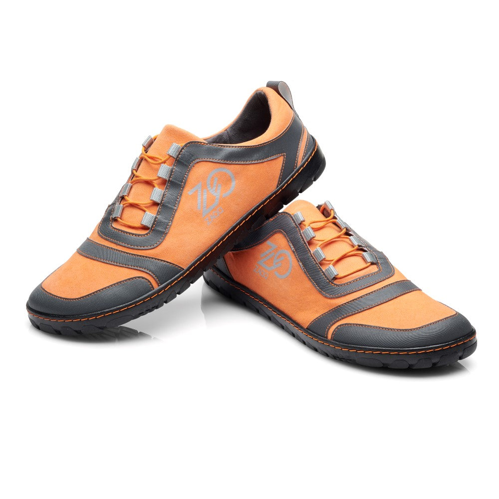 Wir präsentieren den SQILL Orange von ZAQQ: ein auffälliges Paar orange-grauer Sneaker mit weißen Schnürsenkeln und einem markanten Seitendesign. Diese Sportschuhe werden durch eine elegante schwarze Sohle vervollständigt, die sich kunstvoll auf einem weißen Hintergrund abhebt, wobei ein Sneaker stilvoll über dem anderen thront.