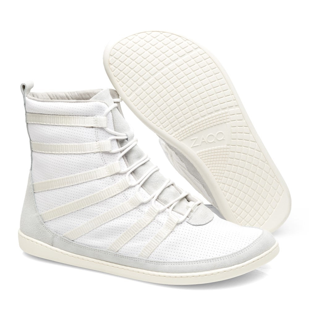 Die SPARQ High White Sneaker von ZAQQ sind aus hochwertigem Nappaleder gefertigt und verfügen über ein perforiertes Design mit mehreren Riemen. Sie verfügen über strukturierte Gummisohlen für hervorragende Traktion. Ein Schuh steht aufrecht, während der andere geneigt ist, um die Sohle zu präsentieren.