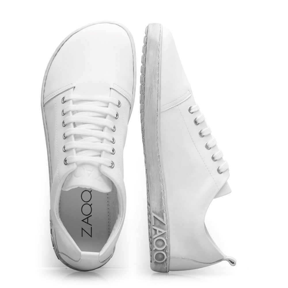 Wir präsentieren den TAQQ Nappa White von ZAQQ: Diese weißen Sneaker sind fachmännisch aus hochwertigem Nappaleder gefertigt und verfügen über klassische Schnürsenkel. Ein Sneaker wird von oben gezeigt, während der andere sein Seitenprofil hervorhebt und das ZAQQ-Branding auf seiner flexiblen Kautschuksohle hervorhebt. Das minimalistische Design steht vor einem schlichten weißen Hintergrund und betont ihre Eleganz.